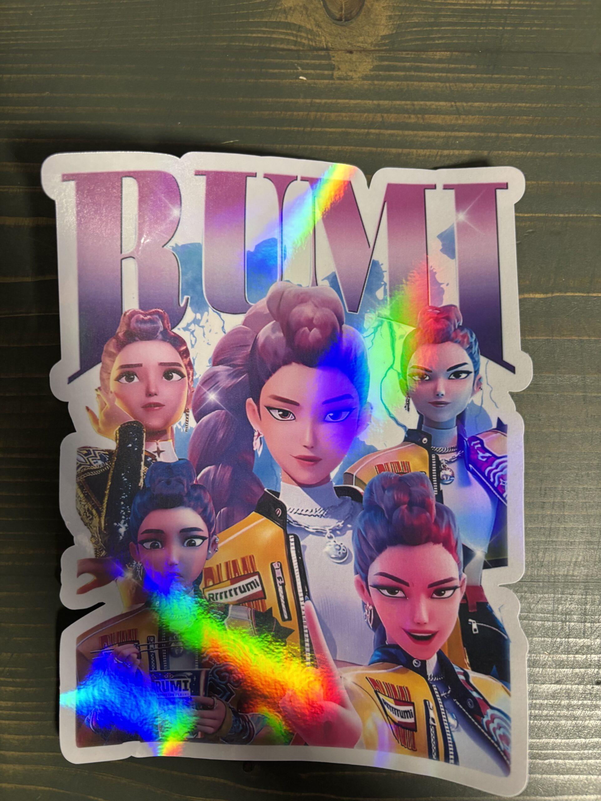 Holografisk klistermærke af en karakter med flere ansigtsekspressioner, iført en jakke med grafik, der viser en farverig regnbue-effekt.